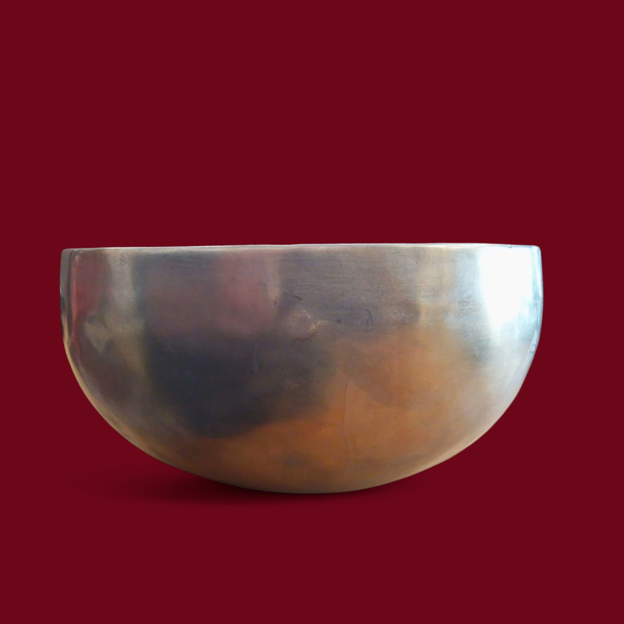 Una grande e lucente Campana Tibetana Nota FA(F) d3 183 HZ -R125/C metallica con base arrotondata si staglia su uno sfondo rosso scuro, evocando la rilassante risonanza di 183 Hz.