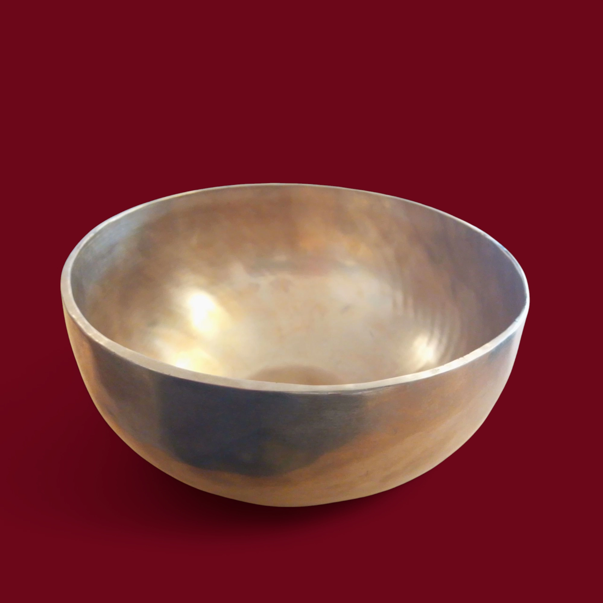 Una Campana Tibetana Nota FA(F) d3 183 HZ -R125/C con una finitura liscia e metallica è appoggiata su uno sfondo rosso scuro e la sua forma arrotondata riflette sottili luci e ombre a 183 HZ nella nota musicale FA.