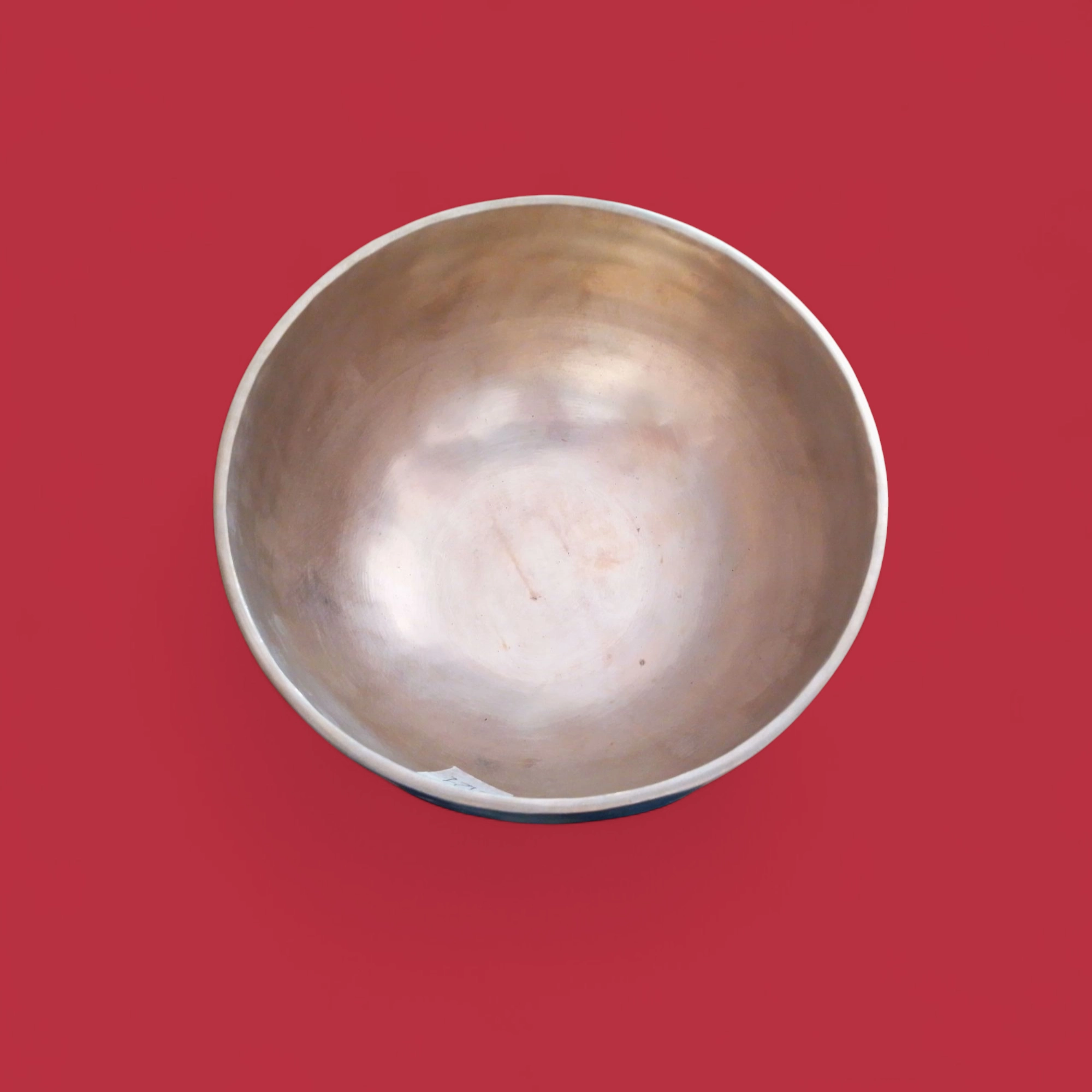 Una Campana Tibetana Nota RE(D) 4 292 HZ -R121/C è posta su uno sfondo rosso uniforme e la sua forma semplice e rotonda in metallo ricorda una classica ciotola tibetana.